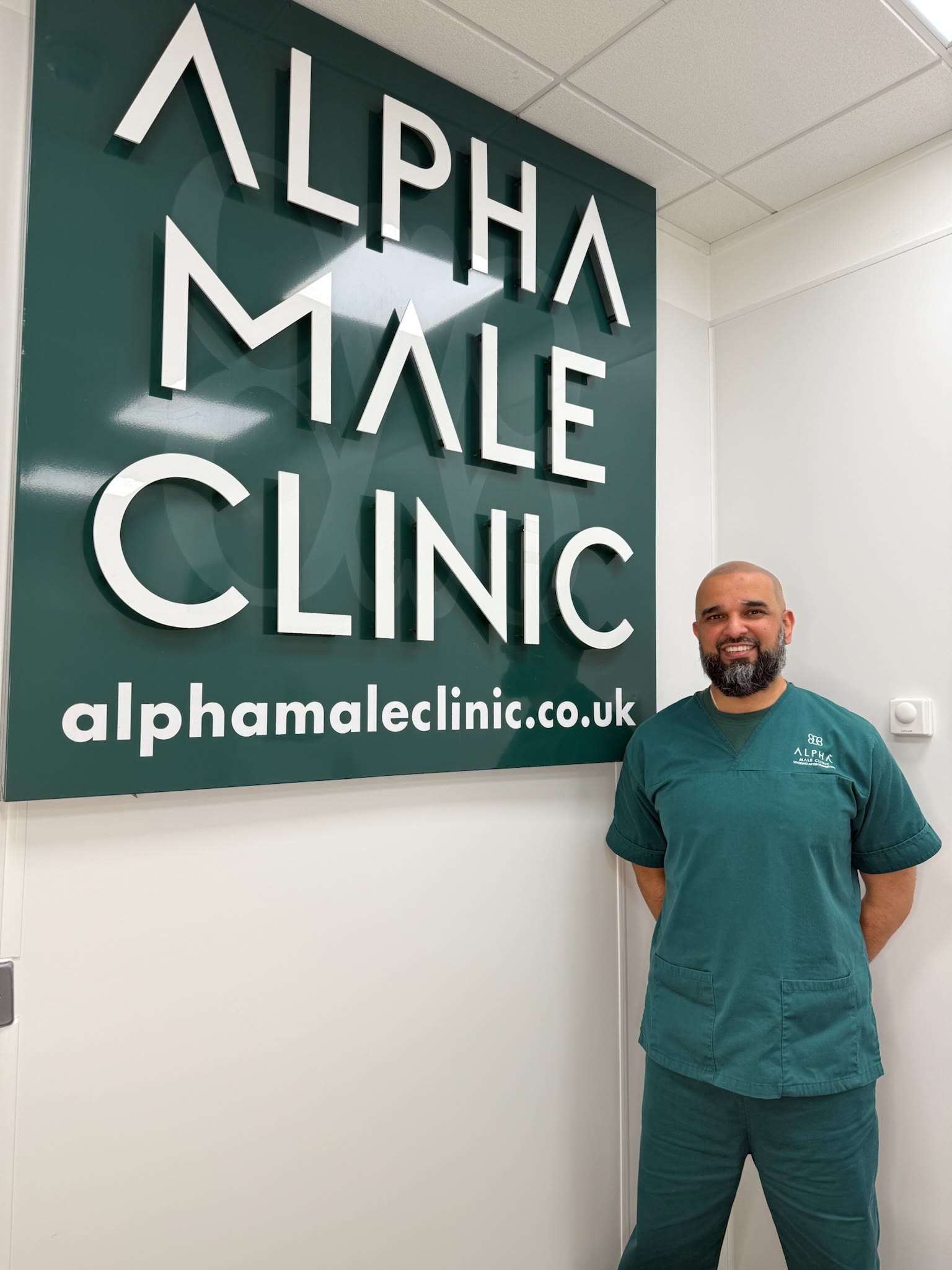 Dr Mustafa Ganijee in clinical scrubs beside the Alpha Male Clinic sign