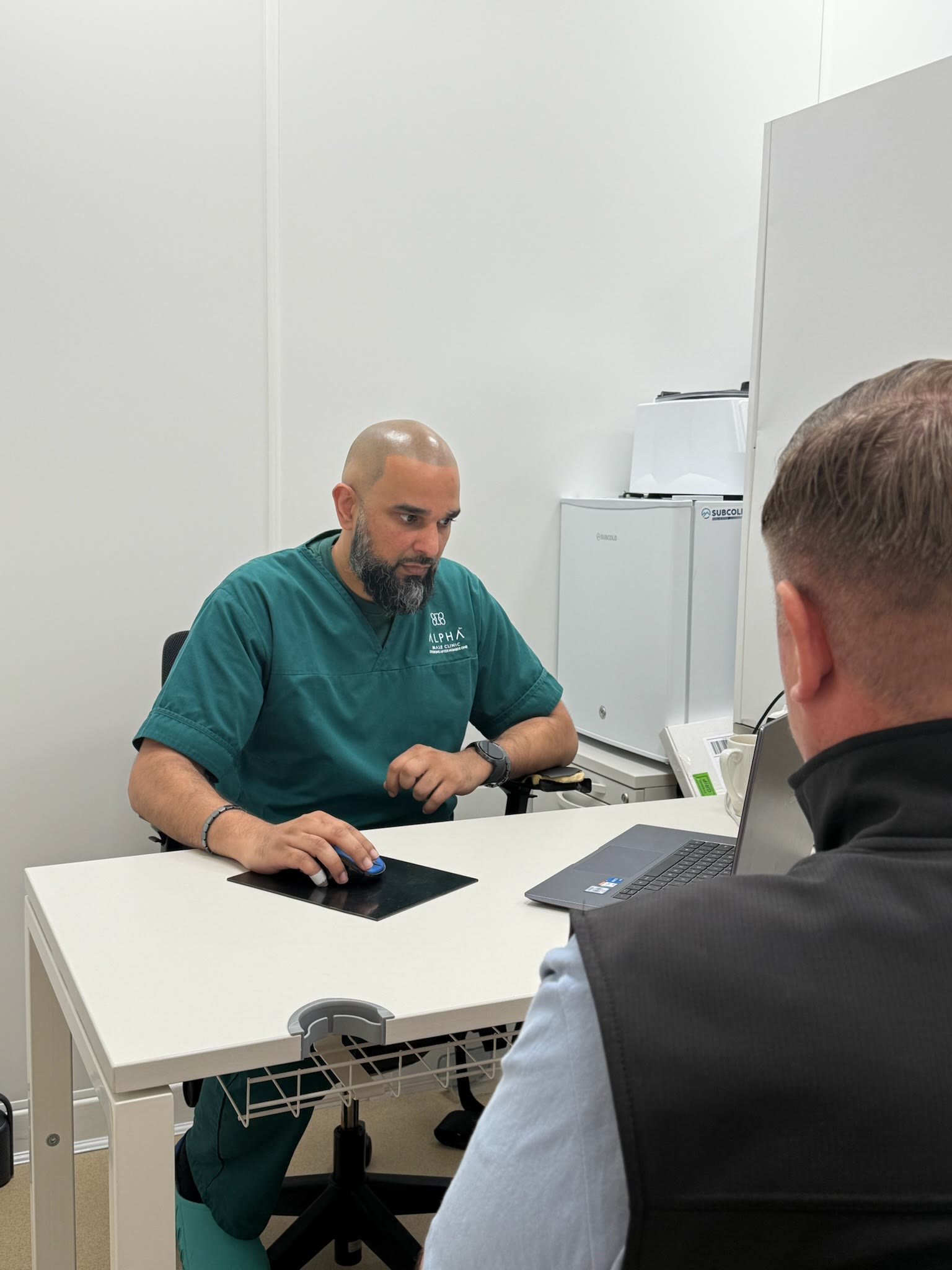 Dr Mustafa Ganijee talking through an assessment with a patient at his desk
